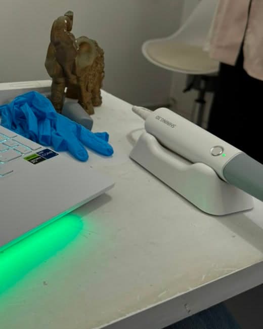 Scanner intraoral sobre a base de carregamento, ao lado do notebook de captura